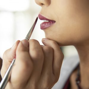Close-up of cosmetician applying lipstick with brush on lips of fashion model