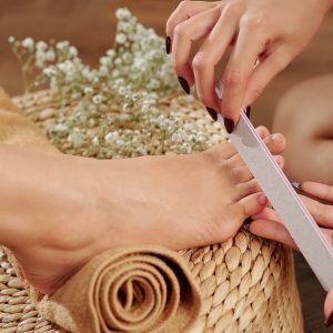 Close-up image of pedicurist filing nails of female client